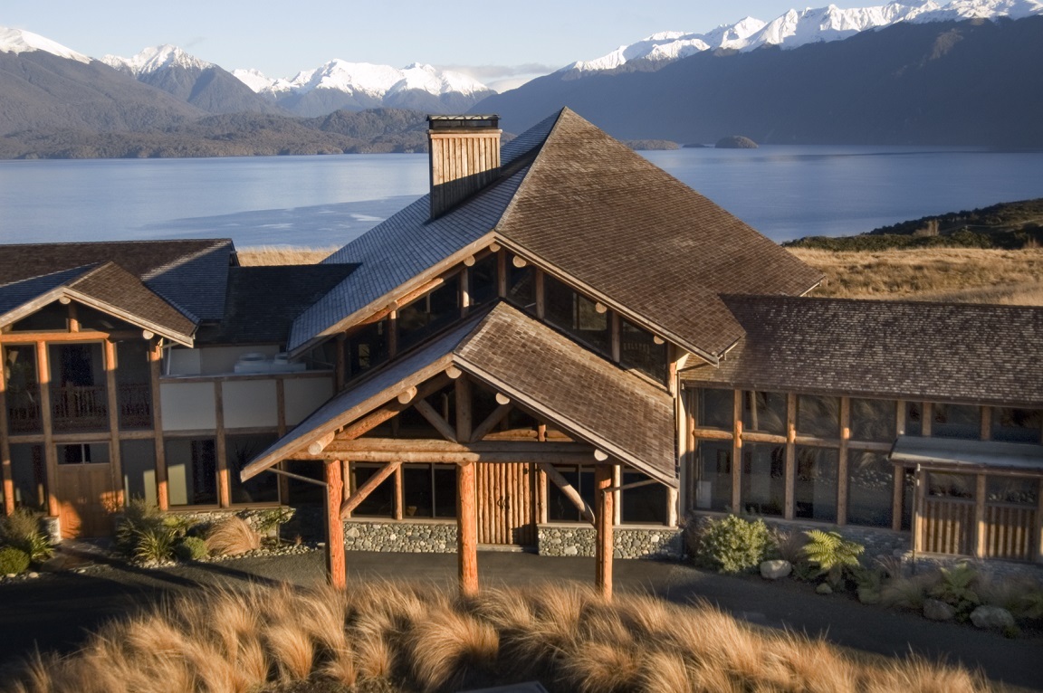Aerial view of Fiordland Lodge showing the main building and grounds on the edge of Lake Te Anau with the Fiordland National Park mountains and bush stretching across the lake to the western shore