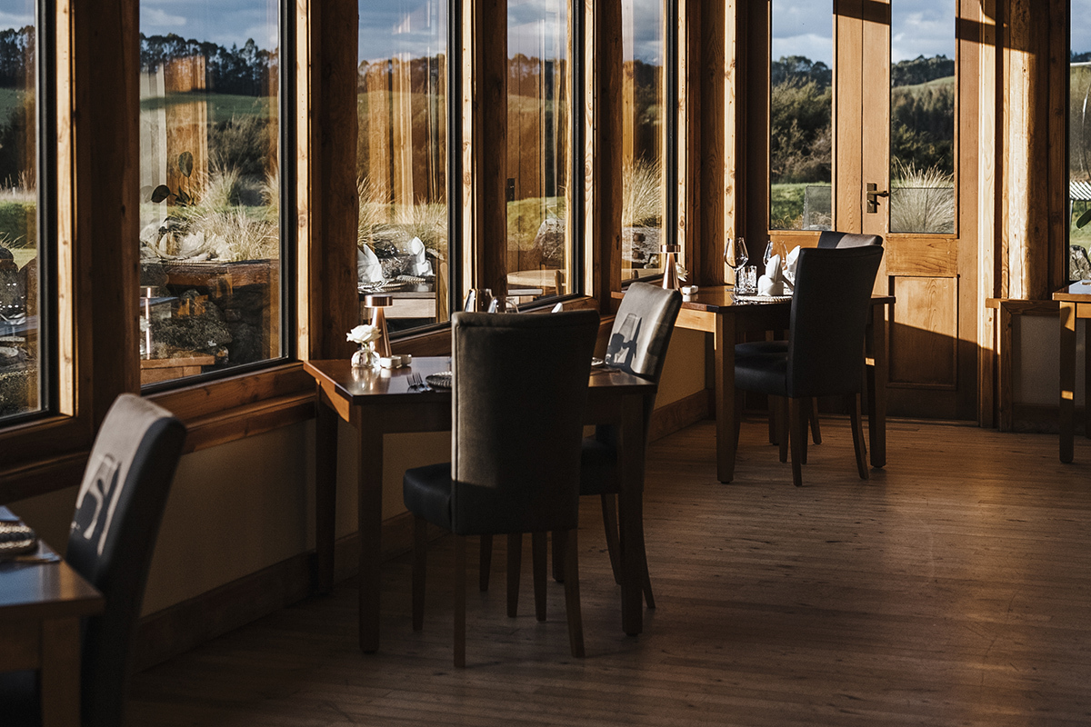 Fiordland Lodge dining room in winter showing the restaurant interior with warm timber detailing and the full sweep of Lake Te Anau and snow-capped Murchison Mountains visible through the floor-to-ceiling windows